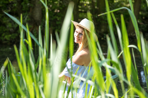 junge hübsche blonde Frau mit langen Haaren genießt ihre Freizeit im grünen Garten im Frühling Sommer an einer Holzhütte auf einer Bank sitzend, mit einer Schiffs Lampe photo