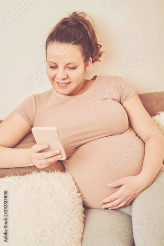 Pregnant woman using cellphone while sitting on sofa at home.