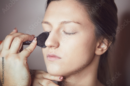 Young beautiful woman applying make-up by make-up artist. Process of making makeup.