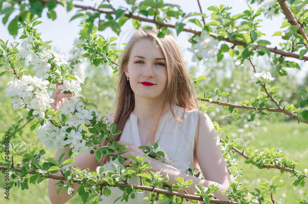 Portrait of a young beautiful woman in white top standing among blooming apple trees on a sunny day. Close-up with space for text. Portrait of a young beautiful woman in white top standing among blooming apple trees on a sunny day. Close-up with space for text.