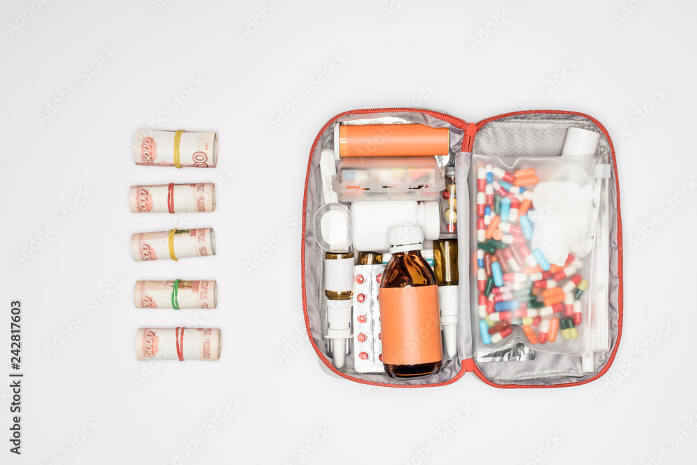 Obraz premium top view of money rolls and first aid kit with medicine isolated on grey