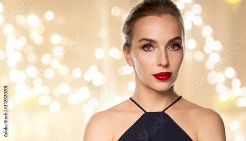people, luxury and beauty concept - close up of beautiful woman in black with red lipstick over beige background and festive lights