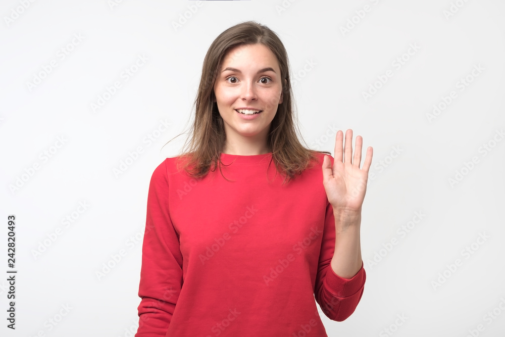 Friendly-looking teenager dressed in red pulover saying hello, waving her hand. Friendly-looking teenager dressed in red pulover saying hello, waving her hand.
