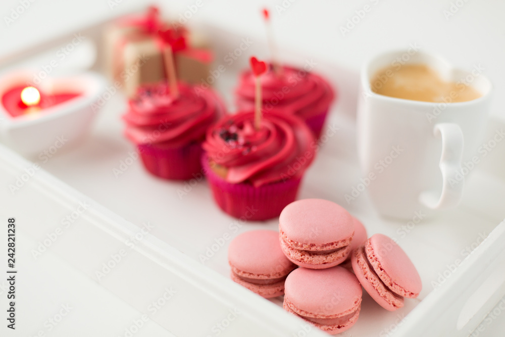 valentines day and sweets concept - close up of pink macarons, frosted cupcakes with red heart shaped cocktail sticks and coffee cup on tray valentines day and sweets concept - close up of pink macarons, frosted cupcakes with red heart shaped cocktail sticks and coffee cup on tray