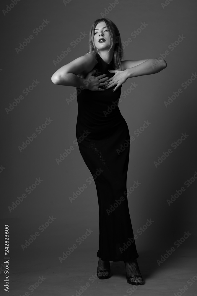 Cute blonde woman in gorgeous, elegant dress.Posing on grey backgorund.Black and white.Studio. Cute blonde woman in gorgeous, elegant dress.Posing on grey backgorund.Black and white.Studio.