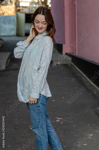 young beautiful girl dressed in a lightweight shirt and light blue jeans poses for a photo in the middle of the street, smiling © Максим Галінский