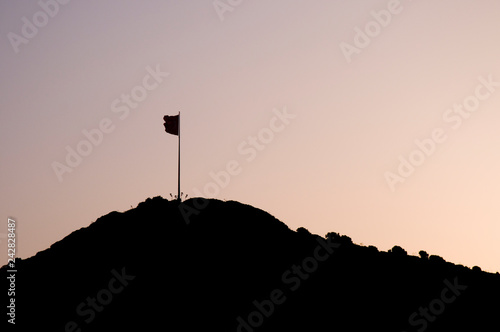 A silhouetted flag isolated on a hillside at sunset with purple orange sky