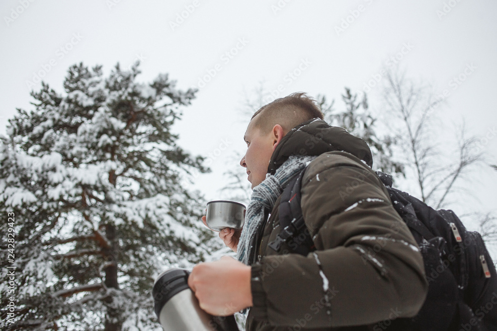 Stylish man with a thermos of hot tea in a snowy conifer forest Stylish man with a thermos of hot tea in a snowy conifer forest