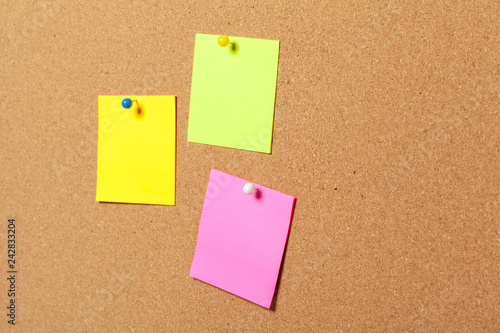 colorful sticky notes with pushpins and blank space, on cork background