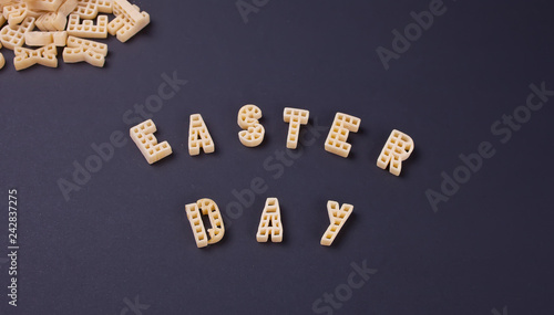 Text Easter day written with macaroni in the form of letters on black wooden table background. Top view.