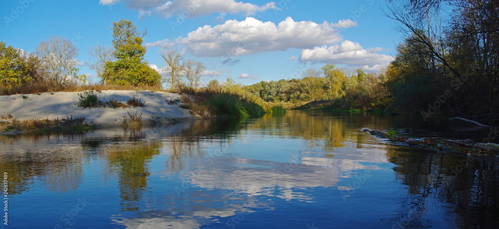 Summer landscape with a flat river and clouds in the blue sky. 