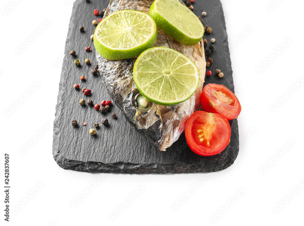 Slate board with grilled dorado fish, lime, tomato and spices on white background Slate board with grilled dorado fish, lime, tomato and spices on white background