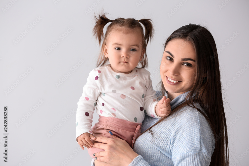 Young mother with her cute little daughter on light background Young mother with her cute little daughter on light background