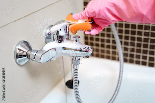 Hand of woman in rubber gloves washing bathtub mixer
