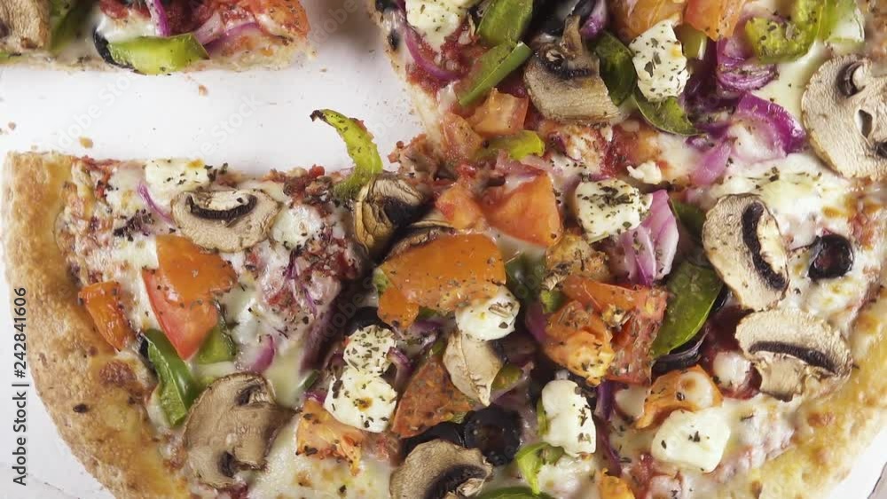 Cut into pieces vegetable pizza with tomatoes and peppers with onions and mushrooms and cheese in a cardboard box rotates counterclockwise top view Cut into pieces vegetable pizza with tomatoes and peppers with onions and mushrooms and cheese in a cardboard box rotates counterclockwise top view