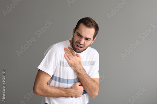 Young man having asthma attack on grey background