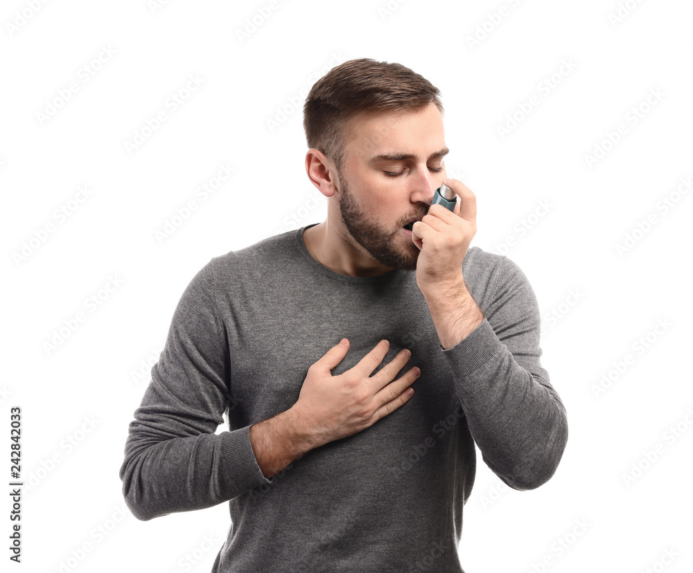 Young man with inhaler having asthma attack on white background
