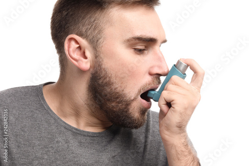 Young man with inhaler having asthma attack on white background