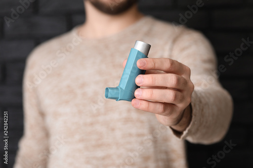 Young man with inhaler on dark background, closeup