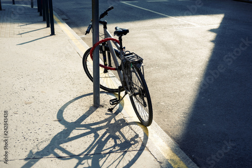 Sunlit sport bicycle leaned to post by the road