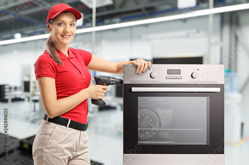 Repairwoman with a drill and oven at a factory looking at the cameraand smiling photo