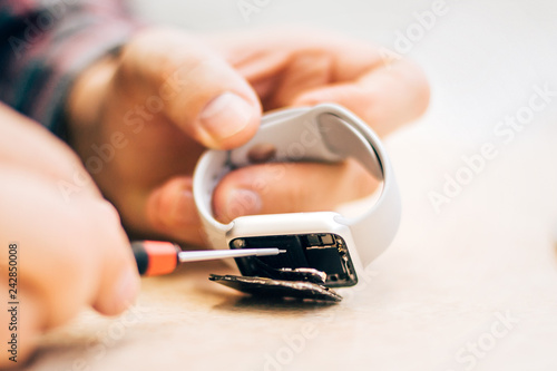 Technician repairs smartwatch with tweezers in electronic smartphone service centar photo