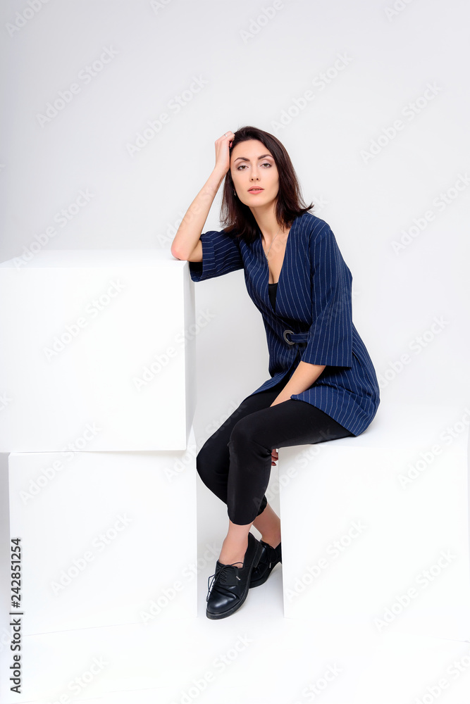 Concept portrait of a girl standing on a white background in a business suit in different poses with different emotions. It in the middle of the frame, next to the white cubes, next is another cube. Concept portrait of a girl standing on a white background in a business suit in different poses with different emotions. It in the middle of the frame, next to the white cubes, next is another cube.