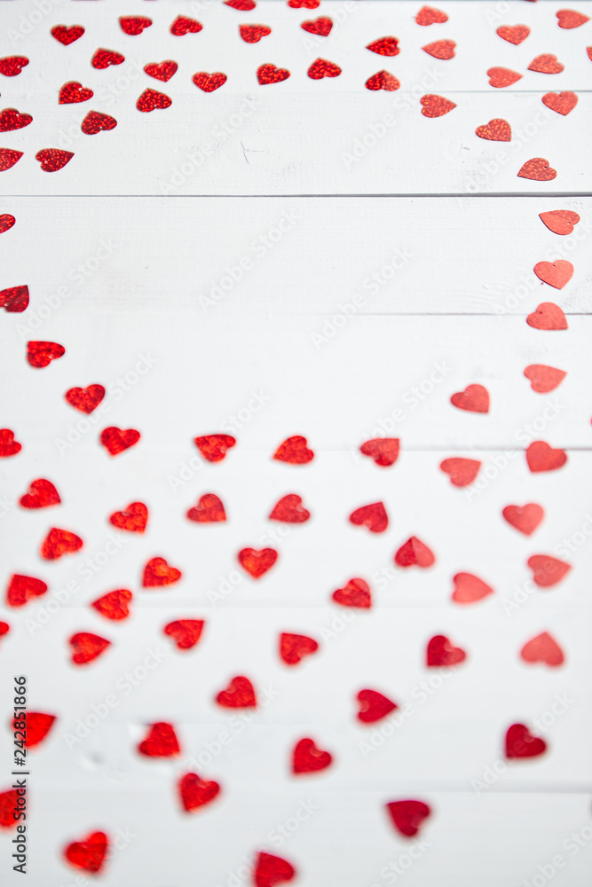Valentine's Day decoration composition. Heart shaped red sequins placed on white wooden table. Frame with copy space. Romantic background. Flat lay, top view.