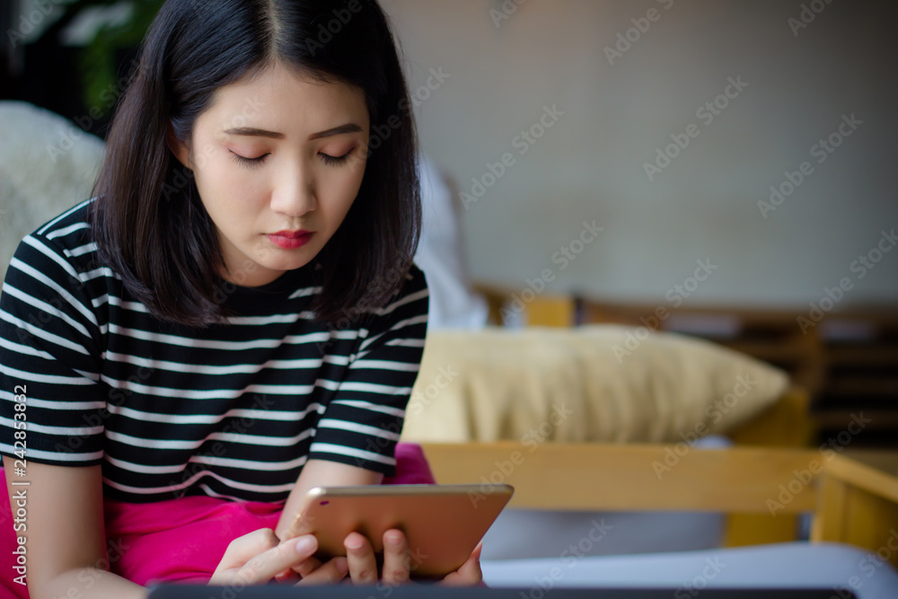 Stressed young professional business woman using tablet computer in Coffee shop. Asian female sitting on couch using tablet ipad surfing, reading message, e-book or internet information in cafe. Stressed young professional business woman using tablet computer in Coffee shop. Asian female sitting on couch using tablet ipad surfing, reading message, e-book or internet information in cafe.