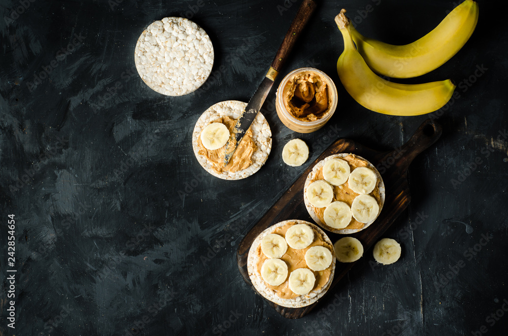 Rice cakes with peanut butter and slices of banana on black wooden table. Space for text. Top view food.