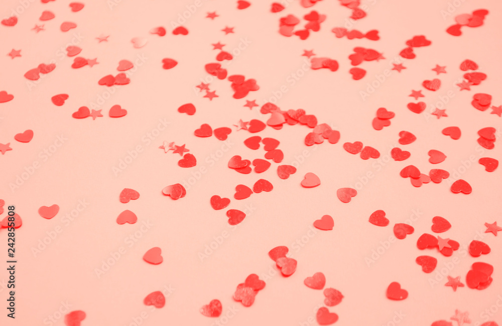 Defocused and blurred beautiful heart and stars shaped red confetti on coral color background.