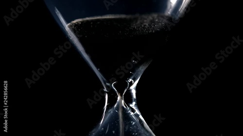 The sand flow in the hourglass with black background and lateral light backlight in centered composition photo