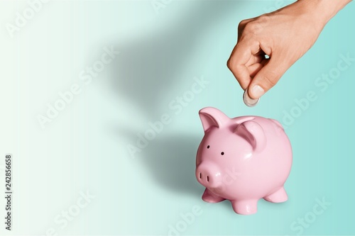 Hand putting coin to piggy bank on blue background