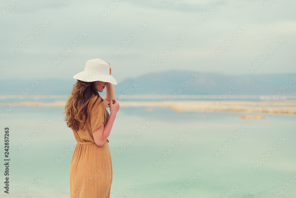 Young girl with shining blonde hair goes to seaside, Dead Sea beach. Banner. Travel, summer vacation, holiday, freedom concept. Digital detox. Sea background, copy space. Young girl with shining blonde hair goes to seaside, Dead Sea beach. Banner. Travel, summer vacation, holiday, freedom concept. Digital detox. Sea background, copy space.