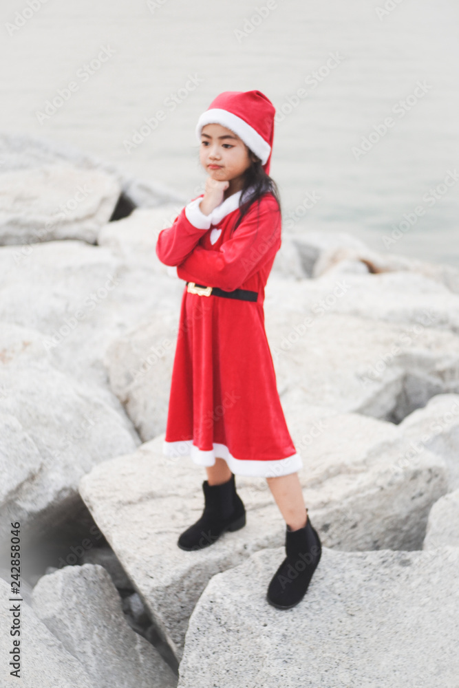 Obraz premium Little Asian girl in Santa Claus dress.Be smiling On the rock dam.