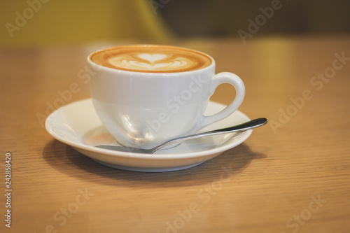 White porcelain cup of coffee with a saucer and a spoon on a wooden table.