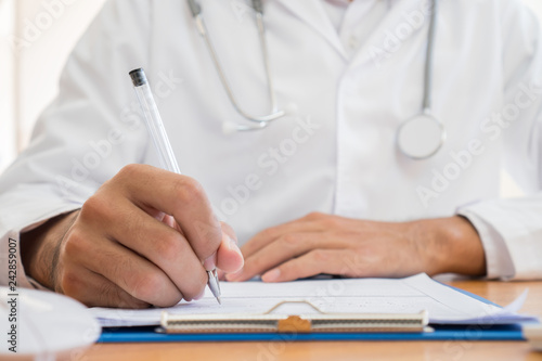 Healthcare medical Expenses concept, Hands Doctor's writing and working on prescription clipboard with record information paper folders on desk in hospital or clinic. Selective focus