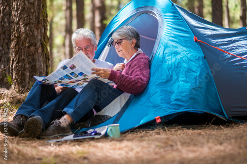 Adult mature retired couple enjouying the wild camping outdoor in the forest looking together a paper map to choose the next adventure destination to see and to live - travel tourism concept photo