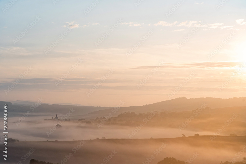 View of village covered in fog during morning sunrise. South moravian landscape with low clouds during a sunrise. Hazy summer scene of small village.
