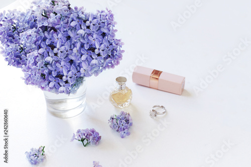 Spring composition with lilac, perfume, lipstick on the table