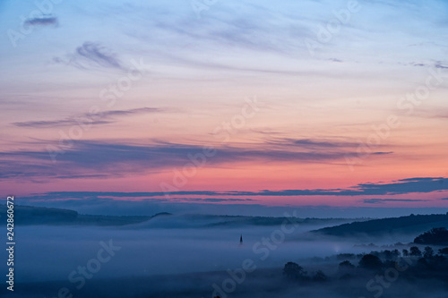 View of village covered in fog during morning sunrise. South moravian landscape with low clouds during a sunrise. Hazy summer scene of small village.