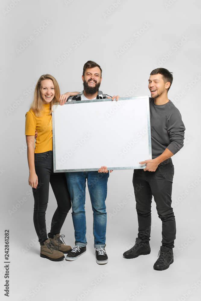 Portrait of three funny laughing young people wearing casual clothes, holding mockup white board isolated in studio, white background Portrait of three funny laughing young people wearing casual clothes, holding mockup white board isolated in studio, white background