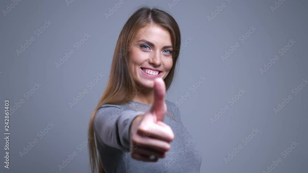 Closeup portrait of cheerful young caucasian female smiling pushing her arm forward and showing thumb up Closeup portrait of cheerful young caucasian female smiling pushing her arm forward and showing thumb up