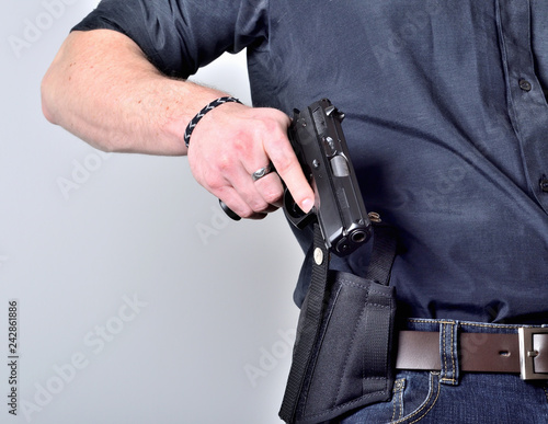 Close-up of man's hand pulling out a pistol gun from the holster on belt, blue jeans, black shirt