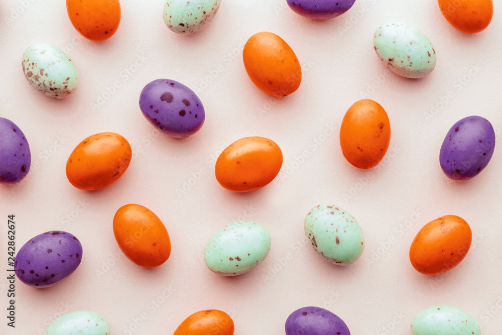 Halloween candy chocolate eggs on a pastel pink background, creative flat lay halloween concept, top view