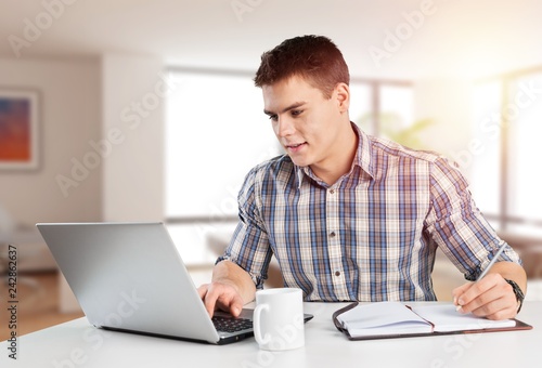 Happy young man works on his laptop with coffee at the table