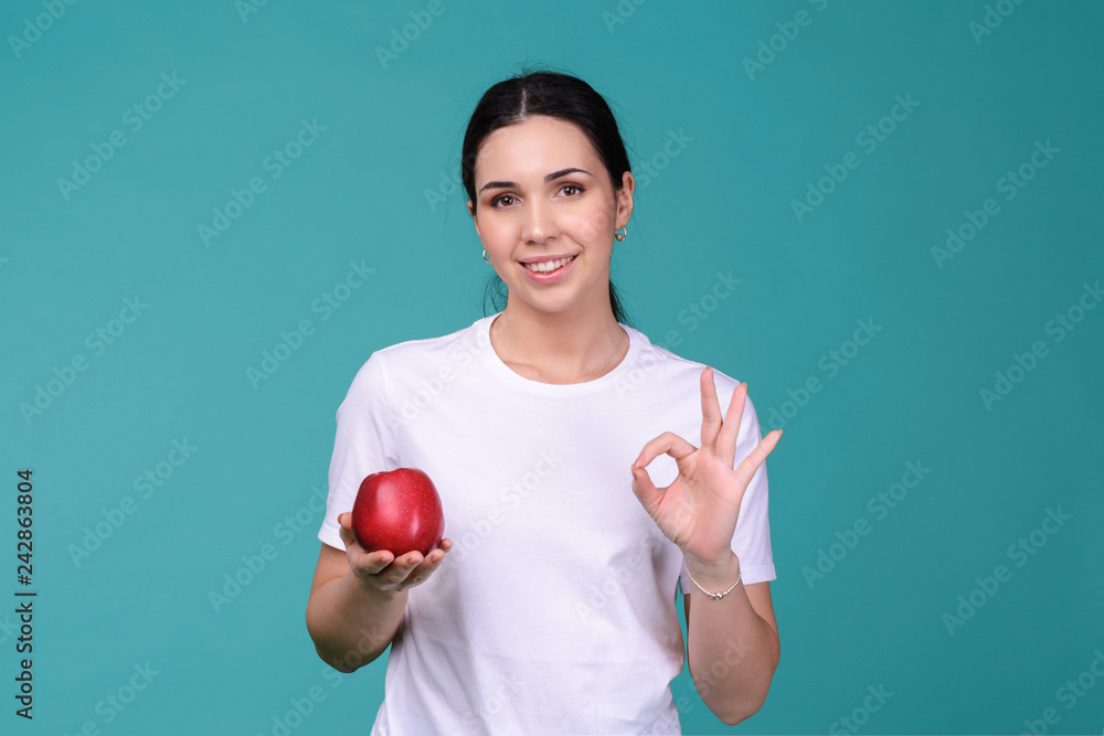Young attractive woman holding a red apple in her hand and show okay sign. Healthy vegetarian food concept. Spring Avitaminosis prevention. Young attractive woman holding a red apple in her hand and show okay sign. Healthy vegetarian food concept. Spring Avitaminosis prevention.