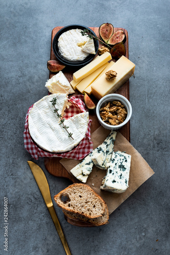 Cheese platter with different cheeses, nuts, bread and dates on a dark background. Retro styled cheese variety selection on dark wood board.