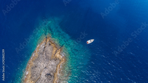 Aerial top view of a deserted island with white boat. Rocky shore of Zannone island near Ponza, Italy. Blue clear water on sunny day.