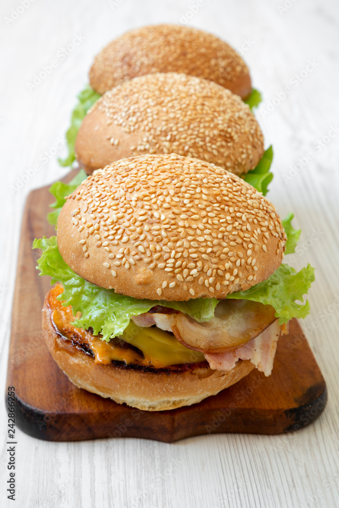 Cheeseburgers on rustic wooden board on white wooden background, side view. Close-up. Cheeseburgers on rustic wooden board on white wooden background, side view. Close-up.